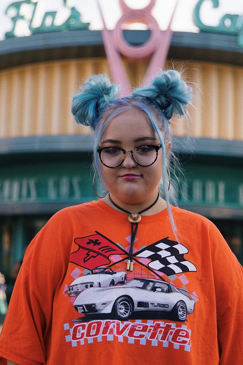 Laurn Godwin posing with her blue double hair bun and orange t shirt