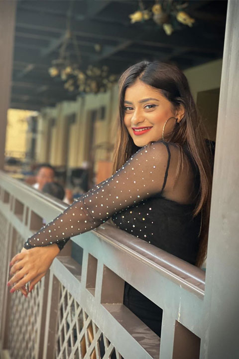 Anam Darbar wearing see through black top and smiling at camera with her perfect red lips and teeth.