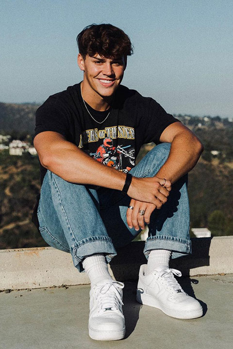 Noah Beck is smiling and looking beautiful in black shirt and blue jeans.